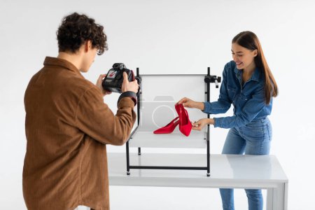 Photo for Professional male photographer and his female assistant doing content photoshoot for shoes, woman styling and helping while working in team in photostudio - Royalty Free Image