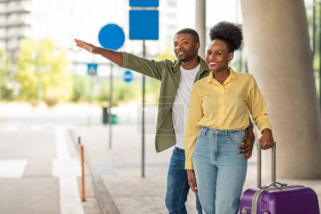 Photo for Cheerful African American Spouses With Travel Suitcase Hailing A Taxi Cab With Hand Gesture Standing Outdoors. Tourists Catching Transport Posing Near Modern Airport Outside. Transportation Concept - Royalty Free Image