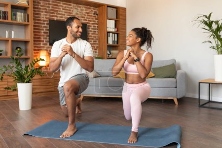 Photo for Smiling handsome young black lady and guy in sportswear doing leg exercises on workout, enjoy fit, energy and sport in living room interior. Stretch, body care, weight loss and active fitness at home - Royalty Free Image