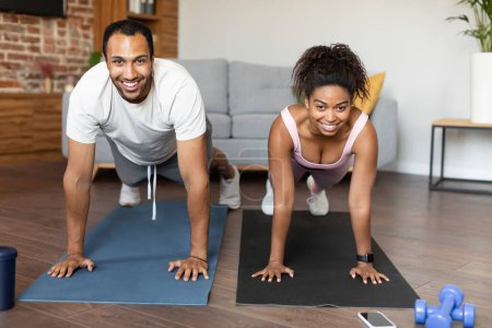 Photo for Sport and fitness for muscle at home. Glad young black couple in sportswear do plank on hands on floor, workout together in living room interior. Body care, weight loss, active lifestyle and vitality - Royalty Free Image