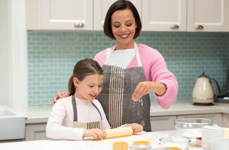 Photo for Cheerful caucasian young mom and little daughter in aprons making dough for cookies with rolling pin and flour in kitchen interior, copy space. Lesson of cook food, homemade sweets at home - Royalty Free Image