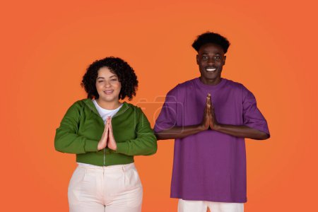 Photo for Relaxation, stress relief, meditation. Cheerful beautiful young multiracial couple folded their hands in front of them and smiling, showing namaste gesture, red studio background - Royalty Free Image