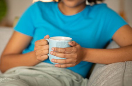 Foto de Millennial mujer afroamericana disfrutar de relajarse y la taza de té en el sofá en el interior de la sala de estar, recortado, de cerca. Descanso nocturno solo, sabrosa bebida caliente fresca y pausa para el café - Imagen libre de derechos