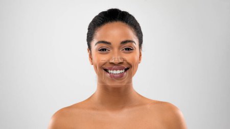 Téléchargez les photos : Portrait d'heureuse belle jeune femme noire à moitié nue souriant à la caméra, posant sur fond de studio gris, démontrant une peau parfaite éclatante, un espace de copie, une bannière. Concept cosmétologie - en image libre de droit