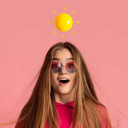 Téléchargez les photos : Choqué inspiré souriant adolescent femme caucasienne en lunettes de soleil avec soleil abstrait au-dessus de la tête isolé sur fond de studio rose. Bonne humeur, émotions humaines positives et offre, réaction sur les bonnes nouvelles - en image libre de droit