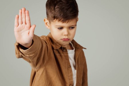 Photo for Sad caucasian 6 years old little boy show stop gesture with hand isolated on gray studio background, close up. Say no, baby whims, kid emotions, childhood and facial expression - Royalty Free Image
