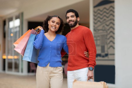 Photo for Great Sales. Smiling Multiracial Spouses Shopping Posing With Paper Shopper Bags Outside, Smiling To Camera. Shot Of Happy Buyers Standing Enjoying Weekend In Modern Mall - Royalty Free Image