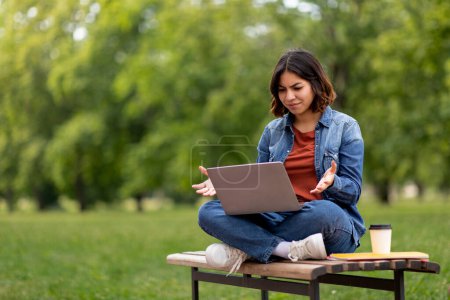 Photo for Confused Young Arab Woman Having Problem With Laptop While Sitting On Bench Outdoors, Middle Eastern Female Student Looking At Computer Screen And Frowning, Suffering Troubles With Distance Learning - Royalty Free Image