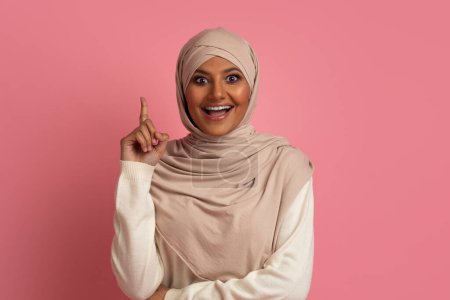 Photo for Excited Muslim Woman In Hijab Having Idea, Pointing Finger Up, Emotional Middle Eastern Lady Wearing Headscarf Having Inspirational Moment While Standing Over Pink Background In Studio, Copy Space - Royalty Free Image