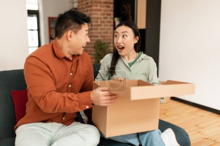 Photo for Emotional korean couple buyers feel overjoyed unpacking cardboard parcel box with internet order, spouses looking at each other, enjoy unboxing shopping online. Shipping, delivery concept - Royalty Free Image