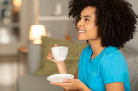 Photo for Satisfied millennial african american curly lady enjoy relax, cup of tea on sofa, look at copy space in cozy living room interior. Good morning, coffee break and silence, evening relax alone - Royalty Free Image