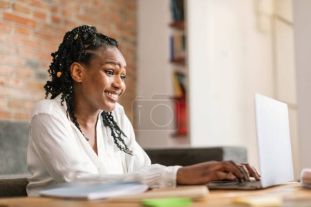 Photo for Smiling african american woman typing on laptop, working or studying online from home, free space. Work, business remotely, freelance at website and new normal at home - Royalty Free Image