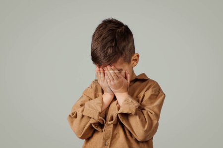 Photo for Sad caucasian 6 years old little kid covering face with hands, crying isolated on gray studio background. Baby whims, negative emotions, childhood, stress and facial expressions - Royalty Free Image
