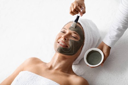 Photo for Beautiful middle aged woman getting skin care treatment at spa center, professional cosmetologist doctor applying anti aging clay mask on face of beautiful mature female, closeup shot, above view - Royalty Free Image