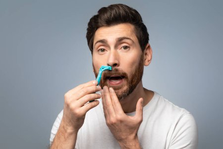 Foto de Hombre barbudo de mediana edad guapo afeitando bigote con navaja y mirando a la cámara sobre fondo gris. Mens cuidado diario y concepto de belleza - Imagen libre de derechos