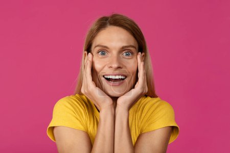 Photo for Shocked happy adult european woman looks at camera and presses her hands to face, isolated on purple background, studio, close up. Amazed offer and ad, huge sale, human emotions and facial expression - Royalty Free Image