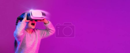 Téléchargez les photos : Incroyable préadolescente expérimentant VR jeu de casque sur fond coloré dans la lumière au néon. Enfant utilisant un gadget de jeu pour la réalité virtuelle. Lunettes futuristes à un jeune âge. Technologie virtuelle - en image libre de droit