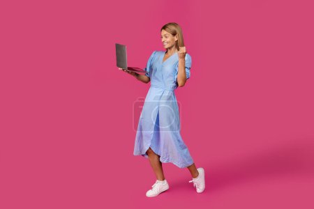 Téléchargez les photos : Femme blonde européenne d'âge moyen joyeuse avec ordinateur portable faisant geste de victoire et de succès isolé sur fond de studio rose. Gadget, émotions positives pour le travail et les affaires - en image libre de droit