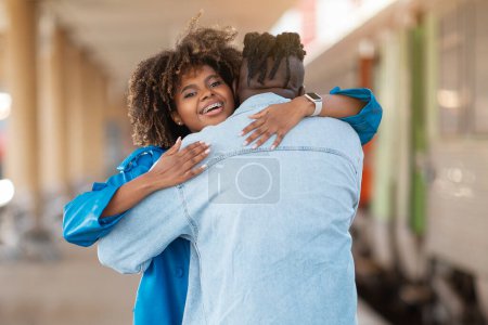 Téléchargez les photos : Joyeux jeune femme noire étreignant son petit ami après la réunion à la gare, Joyeux couple afro-américain embrassant tout debout sur la plate-forme près du train, Gros plan avec de l'espace libre - en image libre de droit