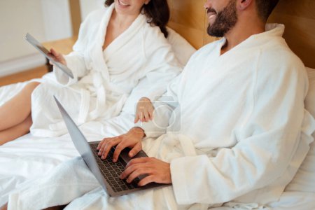 Photo for Cropped Shot Of Couple Using Digital Tablet And Laptop Computers Browsing Internet In Bedroom At Home. Unrecognizable Husband And Wife Working Online Sitting In Bed Indoors. Selective Focus - Royalty Free Image