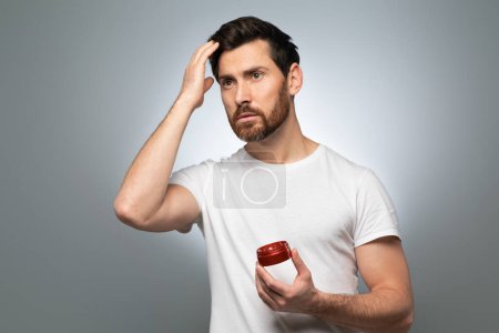 Photo for Pampering, grooming and hair style concept. Portrait of handsome middle aged man fixing touching his hair, holding jar with lotion in hand isolated gray background - Royalty Free Image