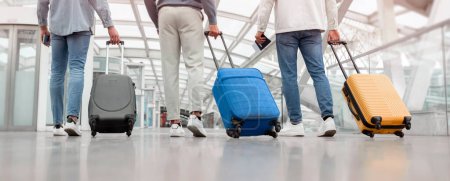 Téléchargez les photos : Voyage. Prise de vue recadrée de trois passagers masculins marchant avec des valises de retour à la caméra dans le terminal de l'aéroport à l'intérieur. Des amis méconnaissables qui partent en vacances avec des bagages. Panorama, Vue arrière - en image libre de droit