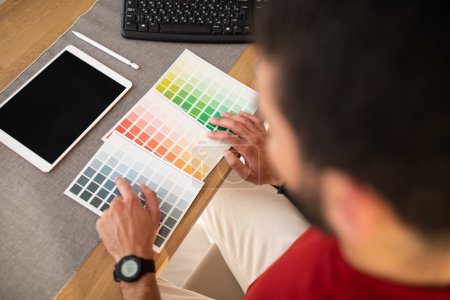 Foto de Diseñador web masculino que utiliza tabletas gráficas en la oficina, vista superior de un empleado irreconocible sentado en el escritorio, comprobando la paleta de colores, bloc de dibujo con pantalla vacía en blanco, maqueta - Imagen libre de derechos
