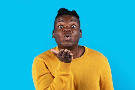 Photo for Young African American Man Pouting Lips And Blowing Air Kiss At Camera, Funny Romantic Millennial Black Male Kissing Somebody While Standing Isolated Over Blue Background In Studio, Copy Space - Royalty Free Image