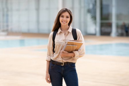 Photo for Cheerful millennial caucasian female brunette student in casual with backpack hold books, enjoy education in campus at university, outdoor. Prepare to exam, study, knowledge, lifestyle in college - Royalty Free Image