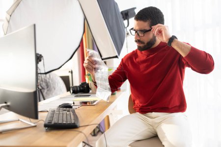 Photo for Serious handsome young hispanic man in stylish casual professional photographer checking photographic flims at fully equipped modern office studio, adjusting his eyeglasses, copy space - Royalty Free Image