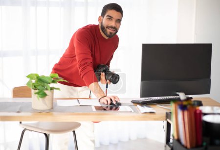 Photo for Professional photographer cheerful handsome bearded hispanic young man working on photo shoot at studio, holding dslr camera, using pc computer, smiling at camera, copy space - Royalty Free Image