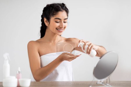 Photo for Attractive Indian Female Using Makeup Remover Lotion And Cotton Pad For Cleansing Skin, Beautiful Young Eastern Woman Making Daily Skincare Routine At Home, Sitting At Dressing Table With Mirror - Royalty Free Image