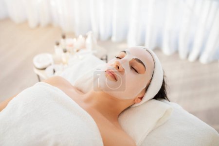 Photo for Woman with facial mask sheet on her face relaxing in beauty salon, calm young attractive female lying with eyes closed, enjoying cosmetologic treatments in modern spa, closeup shot, above view - Royalty Free Image