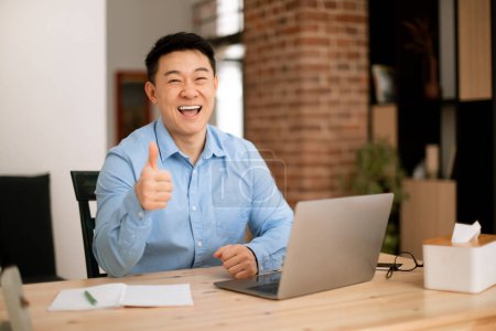 Photo for Happy asian middle aged male freelancer working on laptop from home and gesturing thumbs up, approving remote job, copy space. I like freelance and entrepreneurship - Royalty Free Image