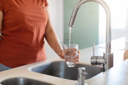 Photo for Thirsty Young Female Filling Glass With Water From Tap In Kitchen, Unrecognizable Woman Pouring Refreshing Drink At Home, Enjoying Healthy Liquid And Taking Care Of Body Hydration, Cropped Shot - Royalty Free Image