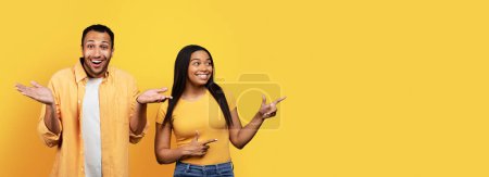 Photo for Confused millennial african american male and smiling wife show to empty space for ad and offer isolated on yellow studio background, panorama. Choice, recommendation, advice and sale - Royalty Free Image