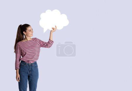 Téléchargez les photos : Joyeux jeune femme hispanique en tenue décontractée tenant une bulle de conversation vierge au-dessus de sa tête sur fond de studio gris, espace libre vierge pour le design, concept de communication - en image libre de droit