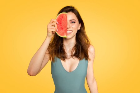 Téléchargez les photos : Concept de l'heure d'été. Jolie femme tenant la moitié de pastèque rouge près du visage, profitant de fruits juteux savoureux, posant isolé sur fond studio jaune vif - en image libre de droit