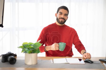 Photo for Portrait of cheerful happy handsome hispanic young man wearing stylish casual outfit photographer posing at workplace, guy sitting at desk with computer, tablet and notepad, drinking coffee - Royalty Free Image