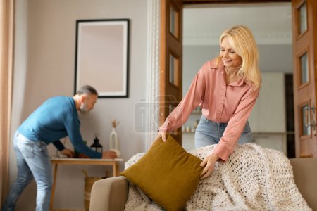 Photo for Spring Cleaning. Mature Couple Tidying Living Room Doing House Chores Together, Dusting Furniture At Home, Wife Putting New Clean Pillow On Sofa. Housework Concept. Selective Focus - Royalty Free Image