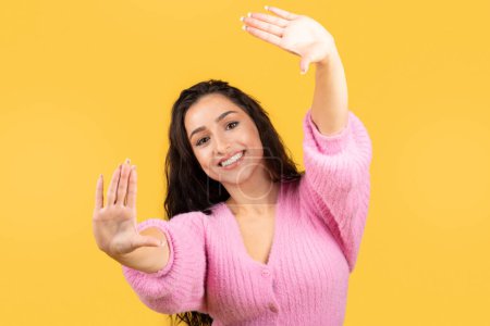 Photo for Smiling millennial middle eastern woman making objective sign with hands isolated on yellow studio background. Art view, creative, take photo, remember moment, lens ad and offer - Royalty Free Image