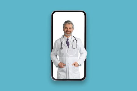 Téléchargez les photos : Joyeux beau médecin d'âge moyen aux cheveux gris debout dans un immense écran de téléphone sur fond de studio bleu, rendez-vous en ligne avec un médecin, concept de télémédecine, collage, espace de copie - en image libre de droit