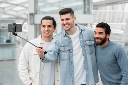 Photo for Three Happy Tourists Guys Making Selfie On Smartphone In Modern Airport, Having Fun Waiting For Flight. Male Friends Posing Taking Photos On Cellphone In Departure Terminal Indoor - Royalty Free Image