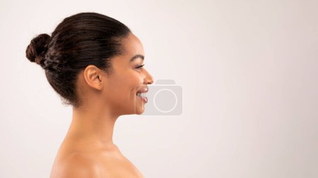 Téléchargez les photos : Portrait de profil de sourire belle femme noire millénariste moitié nue regardant l'espace de copie pour la publicité sur fond de studio coloré, bannière pour la routine de soins de la peau, spa, traitement de massage - en image libre de droit