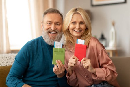 Photo for Cheap Travel Tickets. Happy Mature Couple Showing Their Passports With Boarding Passes Smiling To Camera Sitting On Sofa At Home. Shot Of Joyful Travelers. Vacation Tour Offer Concept - Royalty Free Image
