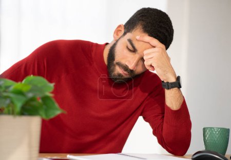 Photo for Closeup of upset tired handsome young businessman hispanic guy in casual outfit sitting at workplace, looking at notepad, touching head, experiencing difficulties in business - Royalty Free Image
