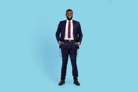 Photo for Portrait Of Handsome Young Black Businessman In Suit Standing On Blue Background, Smiling African American Millennial Male Entrepreneur Looking At Camera While Posing In Studio, Copy Space - Royalty Free Image