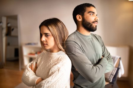 Photo for Angry offended millennial middle eastern boyfriend ignores european girlfriend back to back in living room interior. Divorce, breakup, stress after quarrel, scandal, relationship problems at home - Royalty Free Image