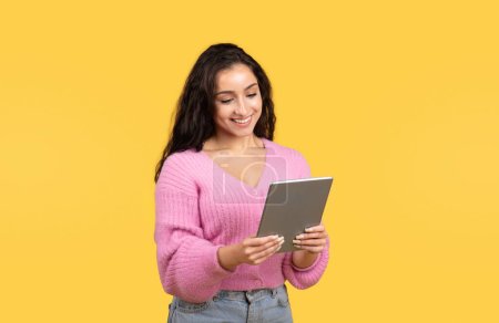 Photo for Happy millennial middle eastern lady manager or student typing on tablet, chatting in social networks, isolated on yellow studio background. Technology for work, study, ad and offer - Royalty Free Image