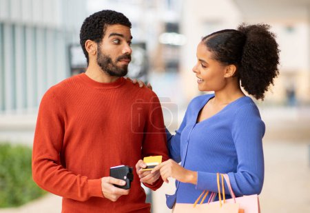 Photo for Stingy Husband. Discontented Man Giving Credit Card From Wallet To His Wife Shopping At Mall Standing Outdoor. Girlfriend Asking Shocked Boyfriend For Money. Financial Dependency Problem - Royalty Free Image